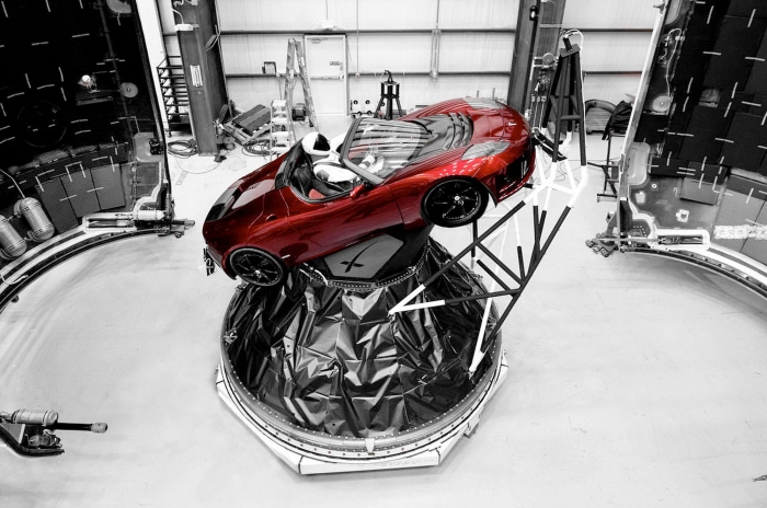 Une voiture rouge avec un mannequin en combinaison spatiale à bord, dans une pièce blanche