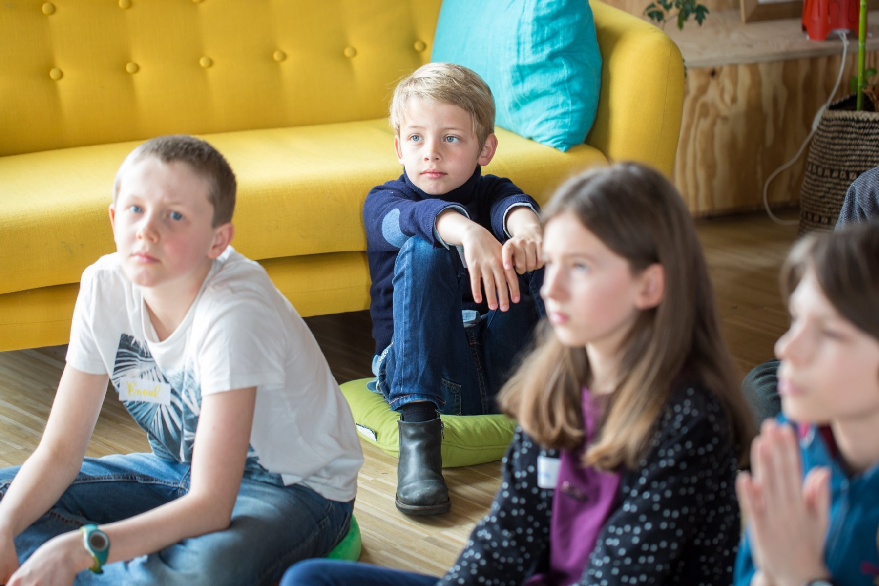 Des enfants sont assis en rond et lèvent le doigt